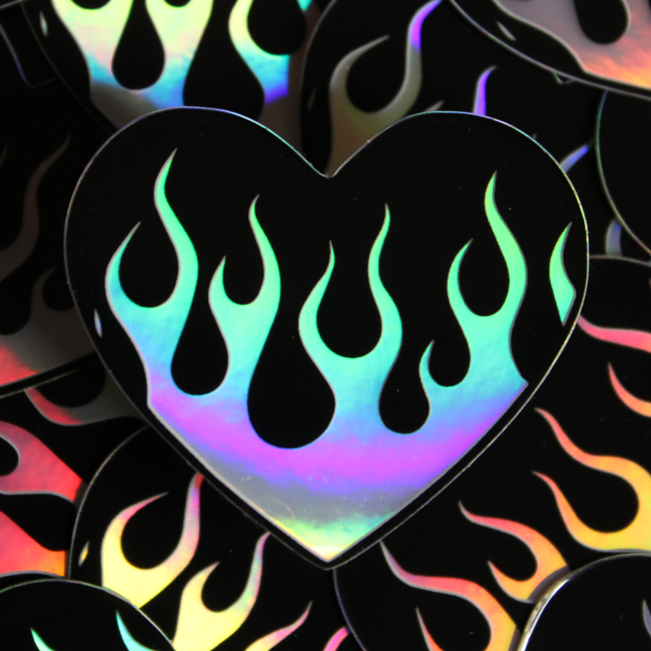 Black heart shaped sticker with holographic flames overlayed in the background and a single one in the foreground